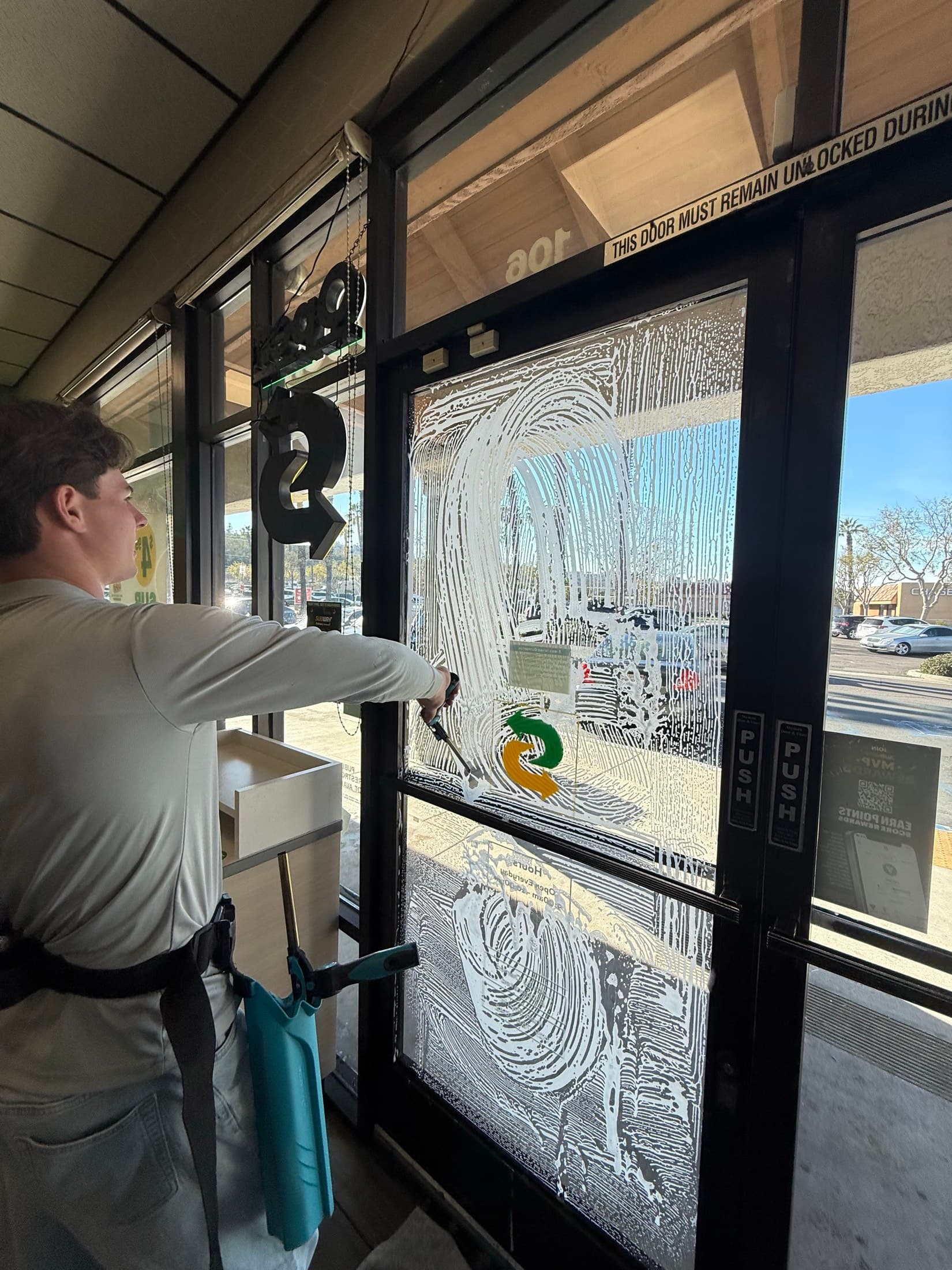 Buxton Window Cleaning technician soaping storefront door glass in El Cajon